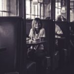 A black and white photo capturing a cheerful girl sitting in a Los Angeles restaurant booth.