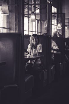 A black and white photo capturing a cheerful girl sitting in a Los Angeles restaurant booth.