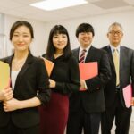 A diverse group of professionals posing confidently in a modern office setting with folders.