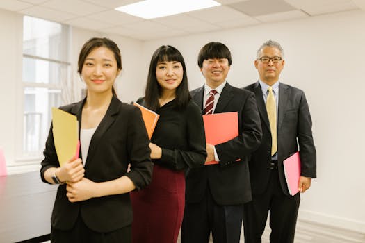 A diverse group of professionals posing confidently in a modern office setting with folders.