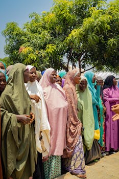 A group of women in colorful hijabs gathering under a tree on a sunny day.