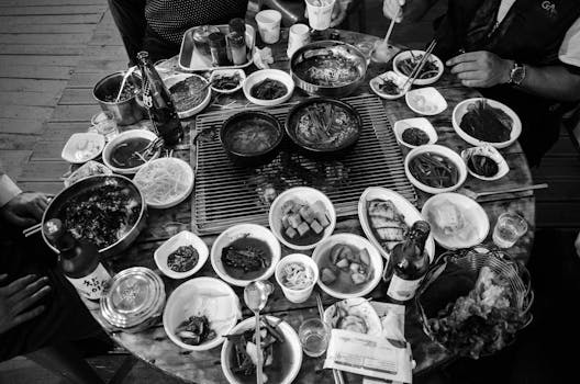 A monochrome image of a diverse Korean dinner spread viewed from above, featuring various dishes and ingredients.