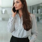 Businesswoman with long brown hair talking on phone in modern office setting.