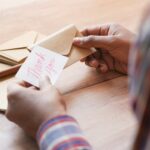 Close-up of hands holding a thank you note in an envelope on a table.