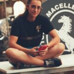 Relaxed young woman in black t-shirt sitting on table outdoors, holding smartphone in Palermo, Sicily.