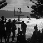 Silhouetted people enjoying a sunset at Manly Beach, Australia, with boats on the water.